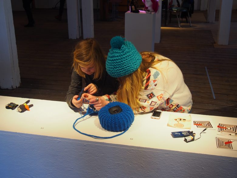 Sam shows off a sonified knitting project to a curious kid.